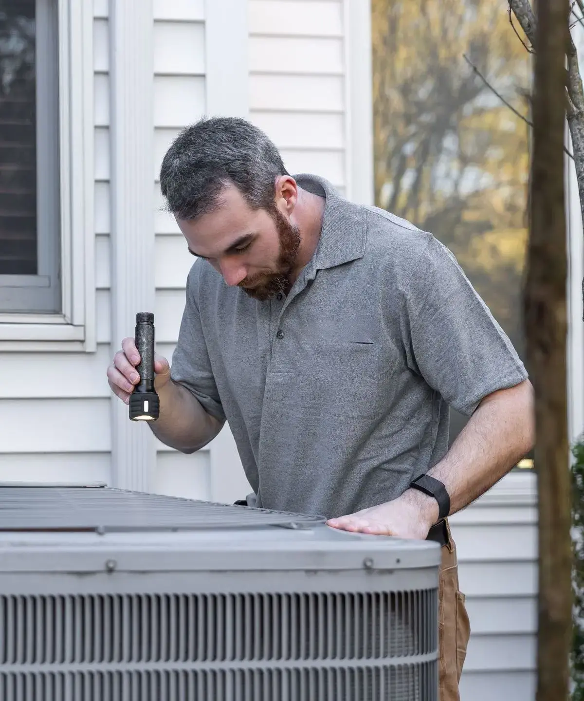 HVAC technician inspecting an outdoor air conditioning unit with a flashlight